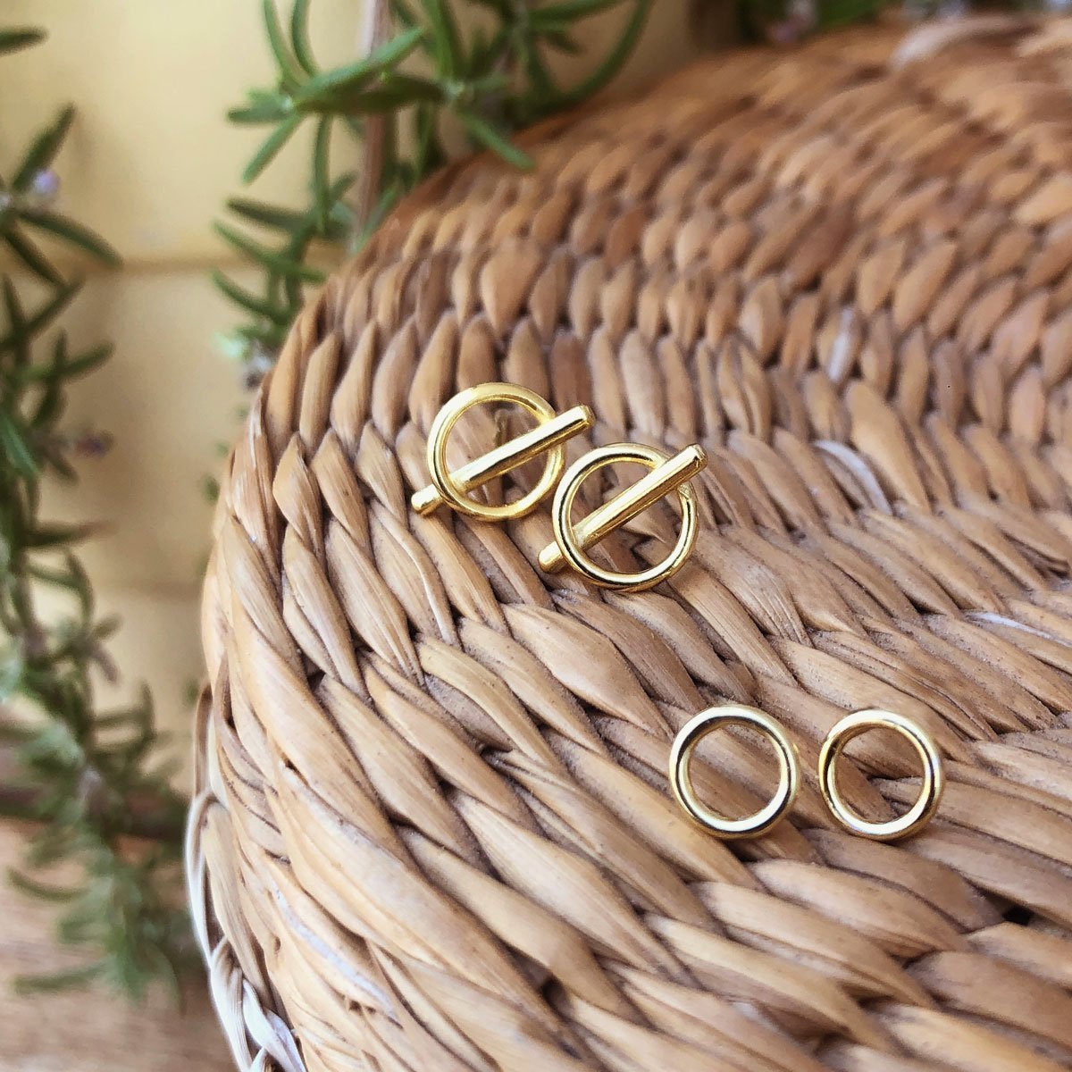 Gold vermeil open circle and bar stud earrings on a woven basket beside rosemary