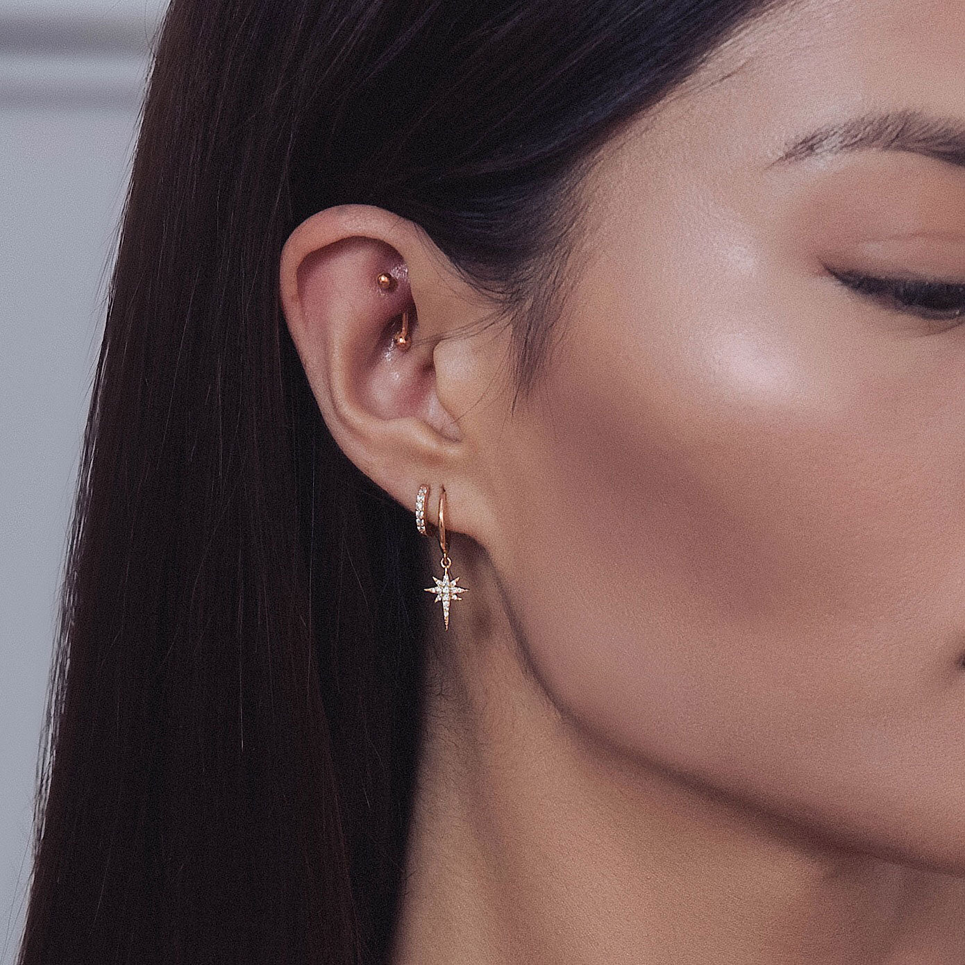 Woman wearing rose gold pave huggie earring and rose gold starburst huggie earrings 