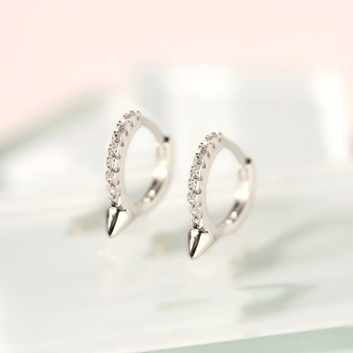 Sterling silver pavé spike huggie hoops with clear stones, shown on a pale prop surface
