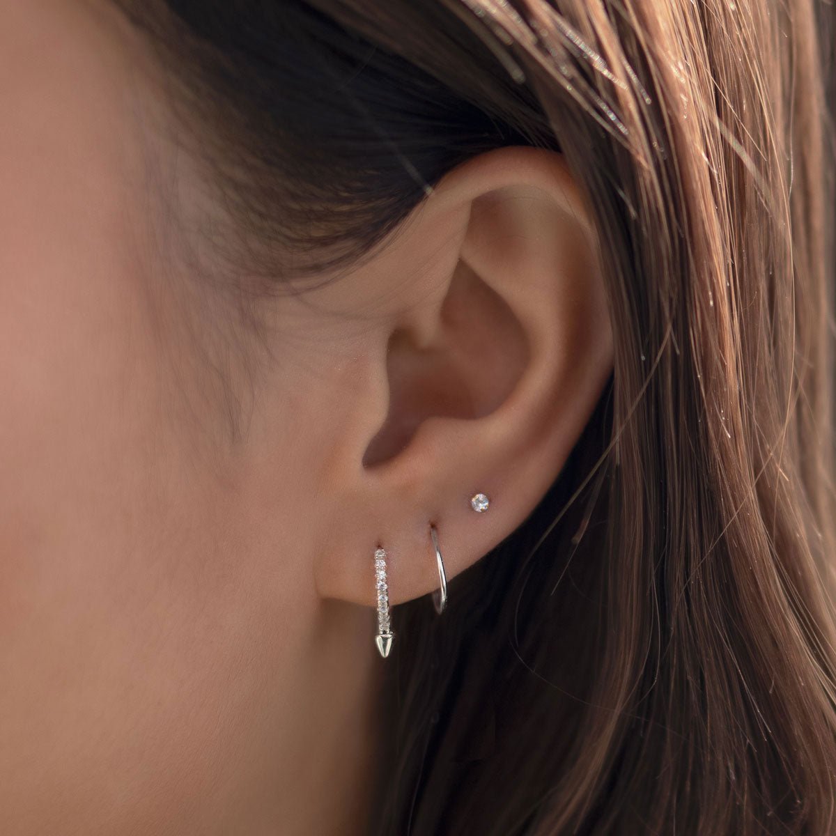 Sterling silver pavé spike huggie hoop with a clear stone row, shown on a model's lower lobe