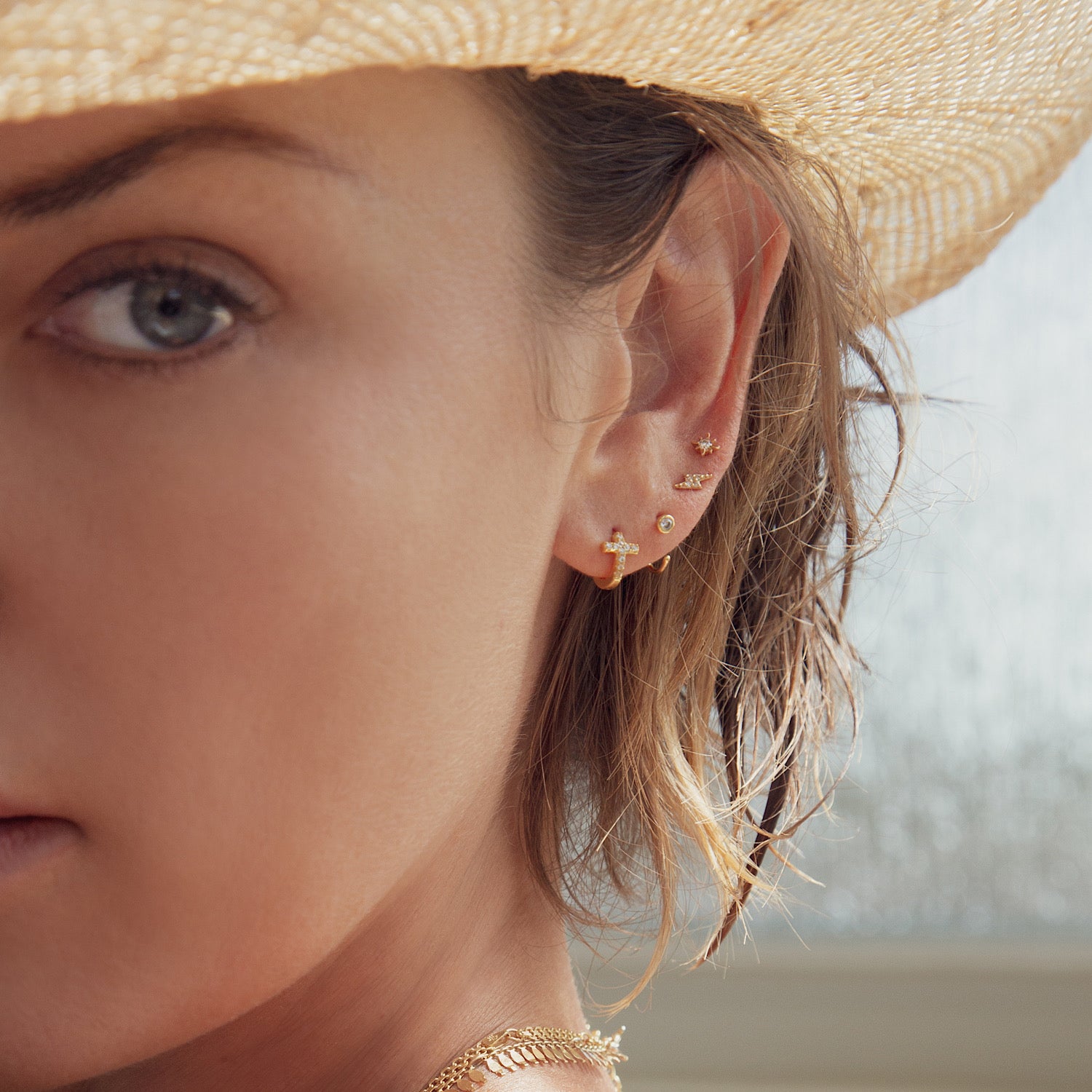 14K gold solitaire huggie with clear zirconia, styled in an ear stack on a model