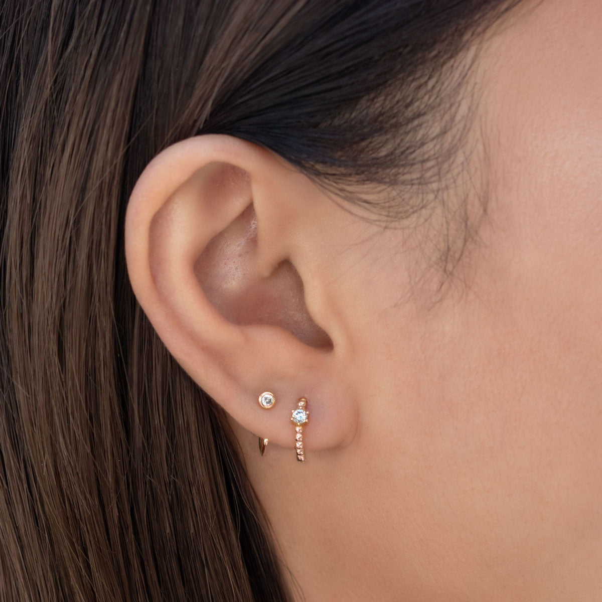 Rose gold vermeil solitaire huggie with a clear zirconia stone, shown on a model's lower lobe