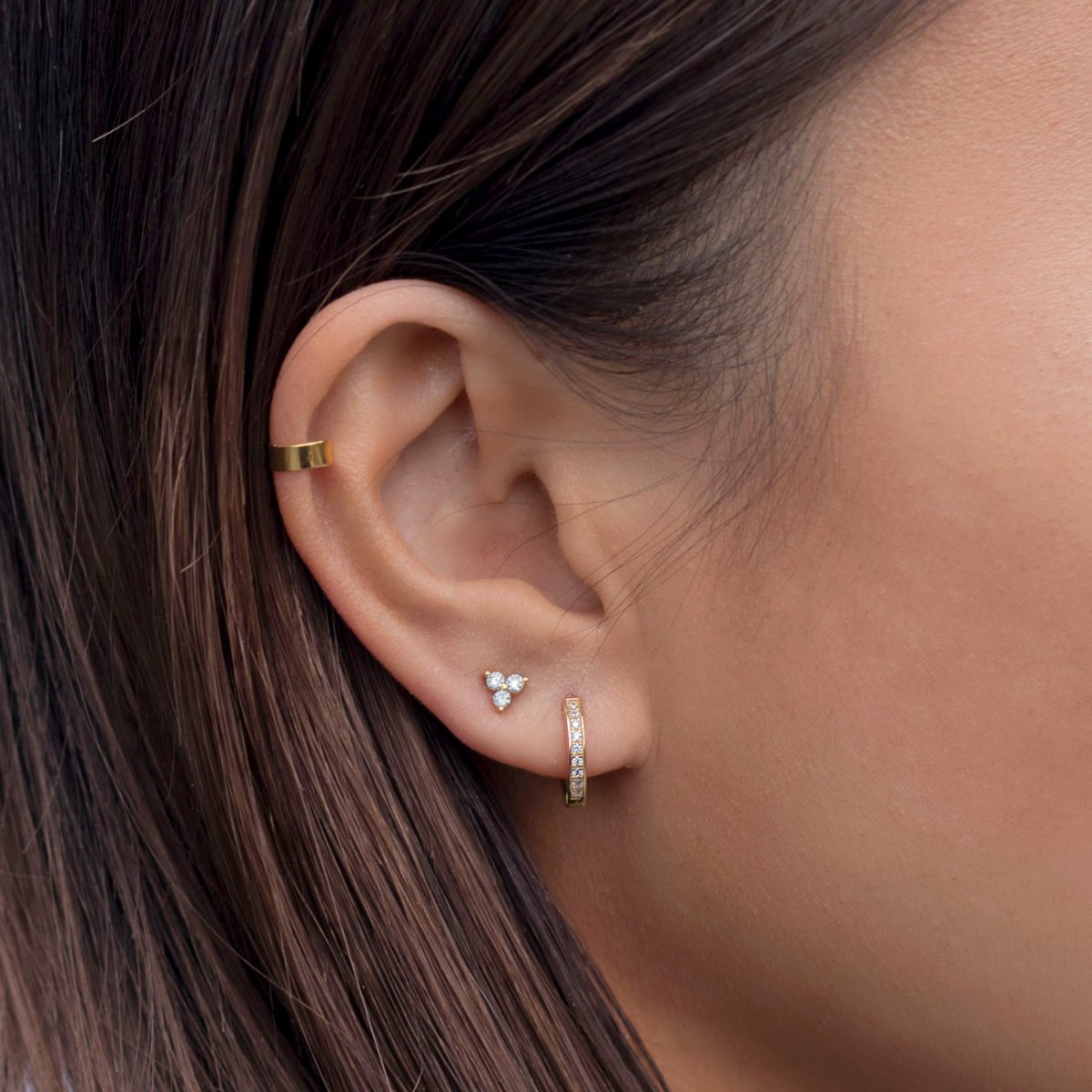 Gold trio cluster stud and pavé huggie hoop shown on a model's lobe