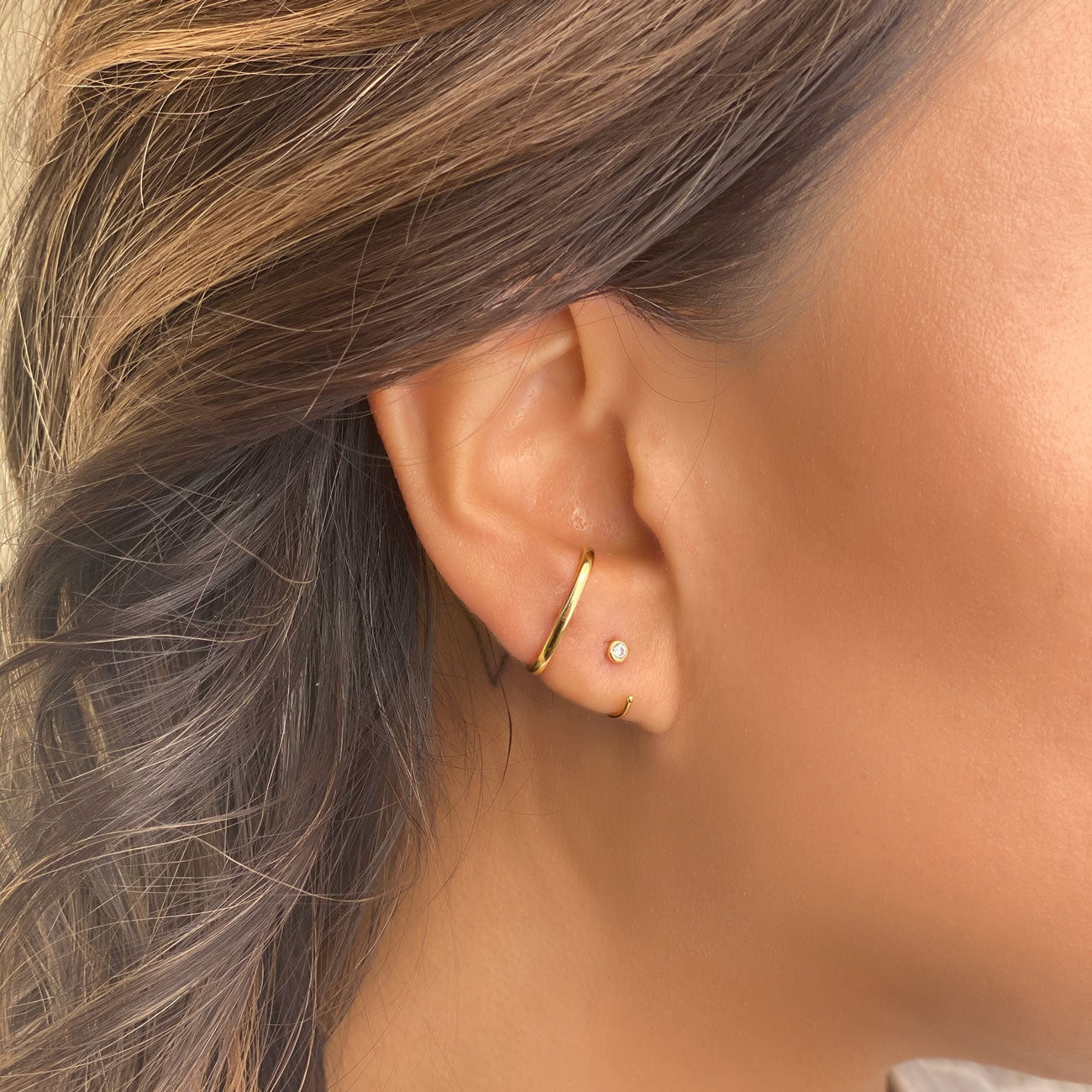 14K gold thin solitaire huggie hoop with a small clear zirconia stud, shown on a model's lobe