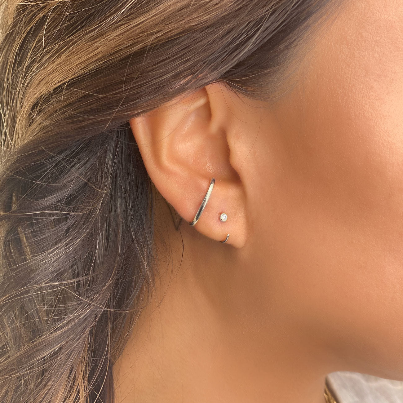 Sterling silver thin solitaire huggie hoop with a small clear zirconia stud, shown on a model's lobe