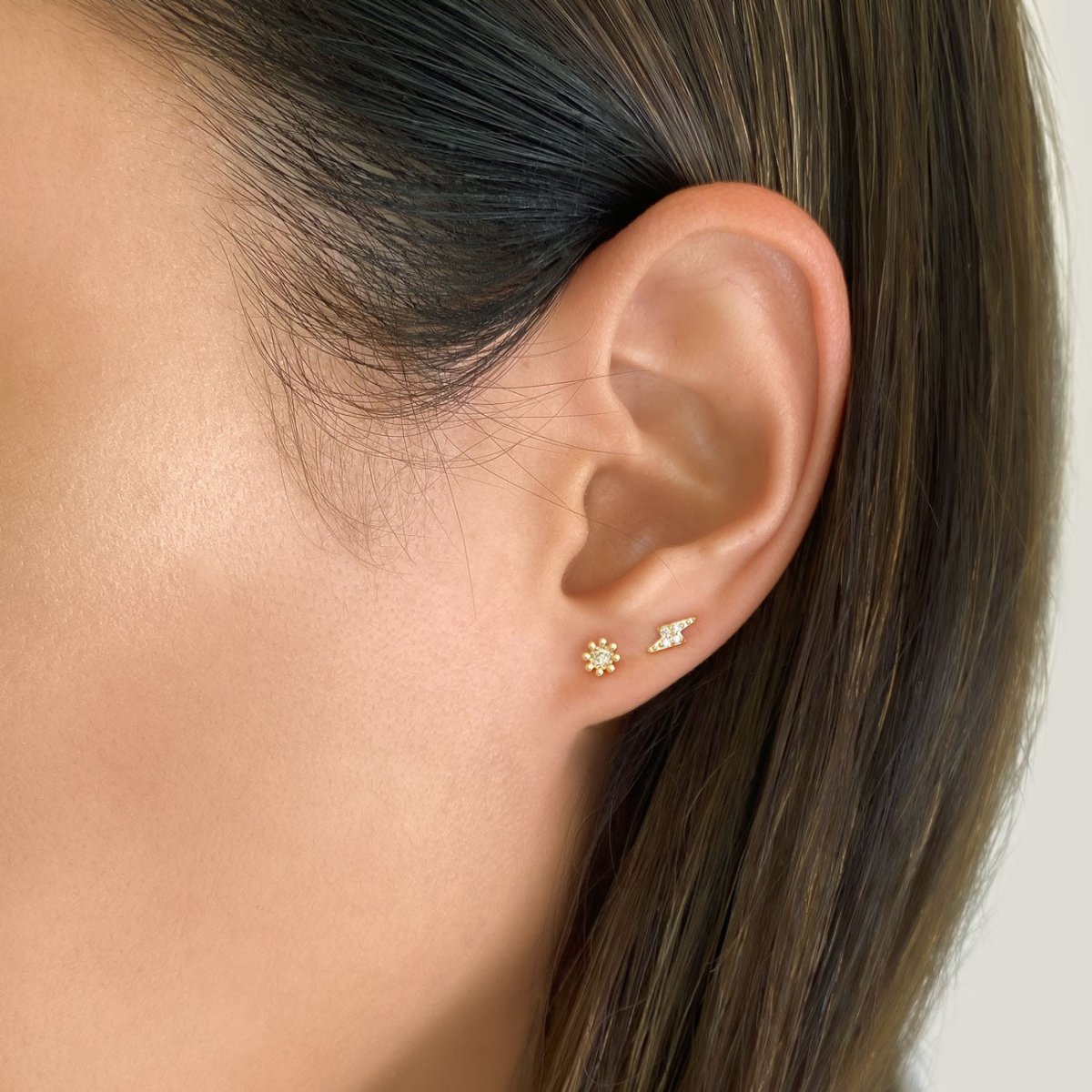 14K gold fleur diamond stud on a model's lobe beside a tiny lightning bolt stud