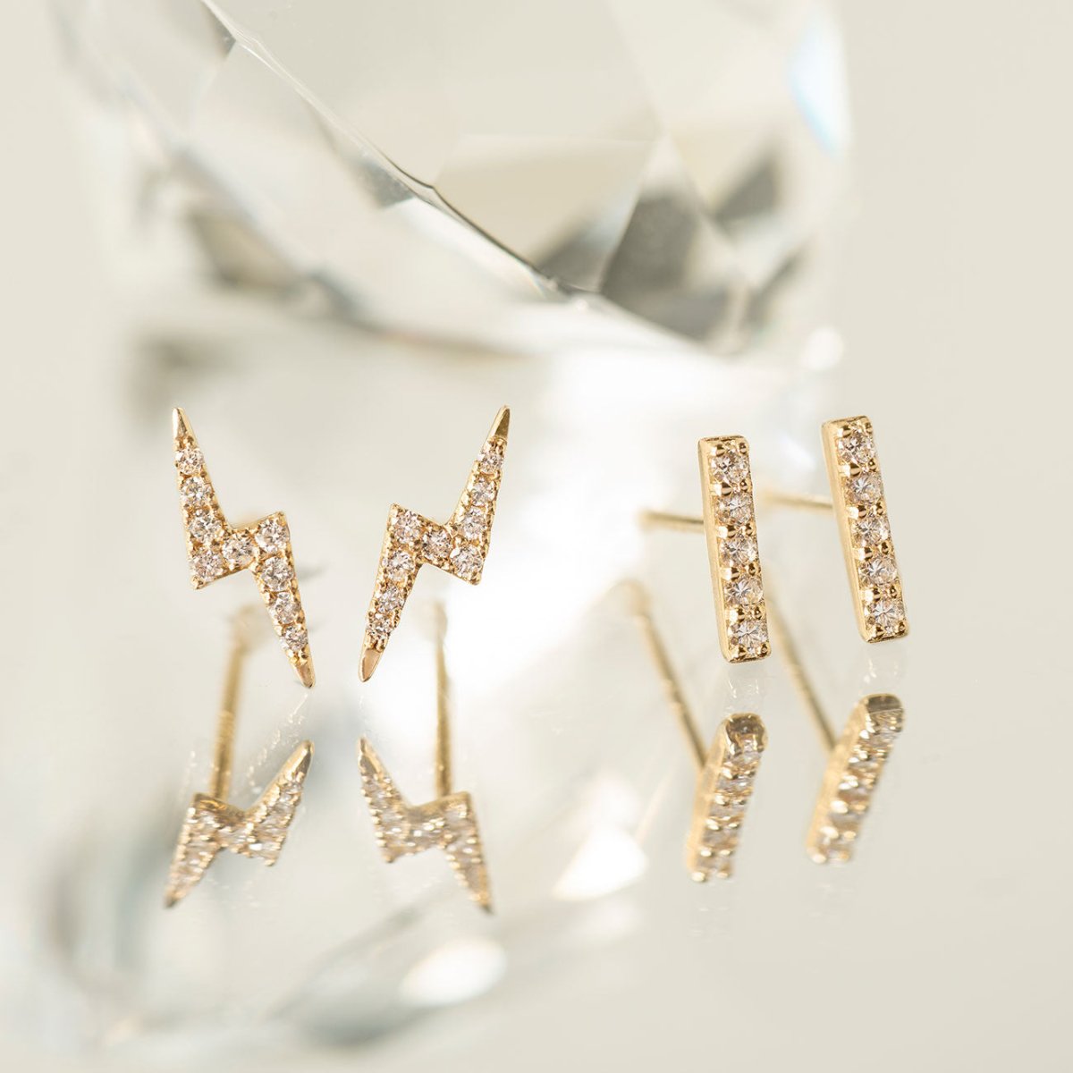 14K gold diamond lightning bolt and bar studs styled beside a clear faceted crystal