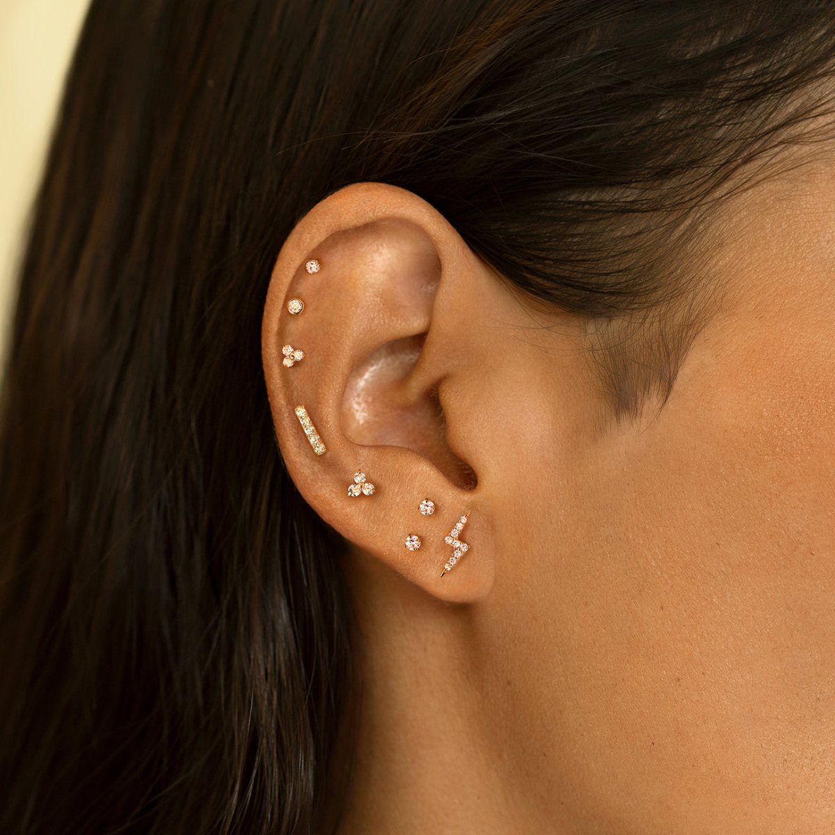 Gold clover and lightning bolt studs shown styled in a cartilage stack on a model's ear