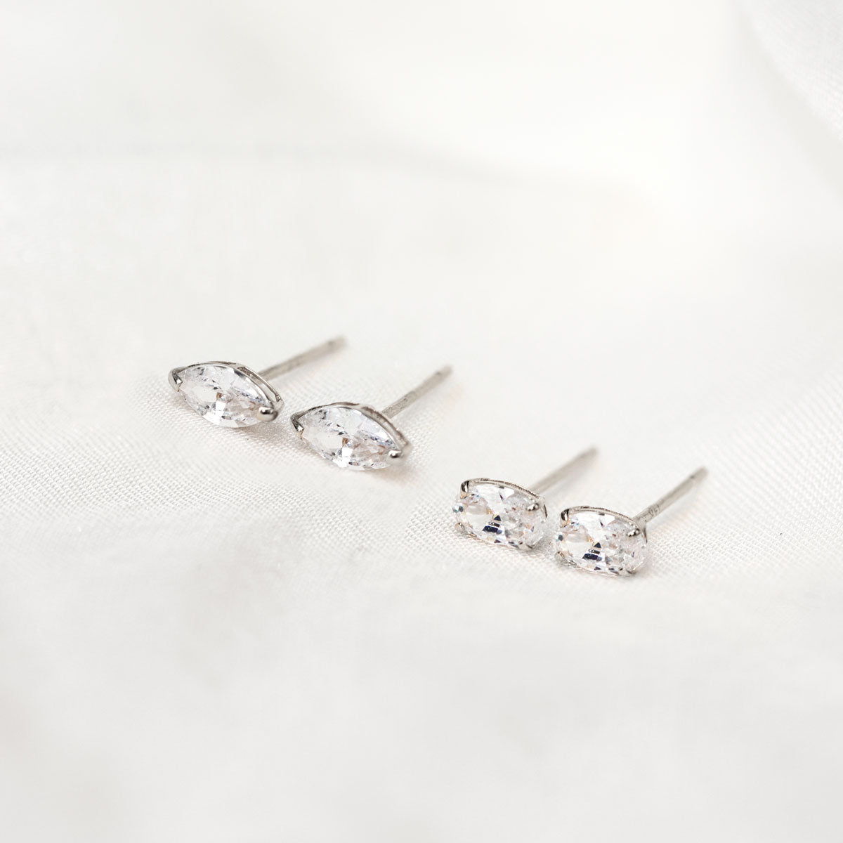 14K white gold studs with clear marquise and oval white zirconia stones, on cream fabric