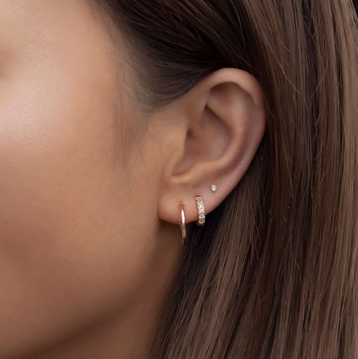 14K gold diamond pave huggie hoop with a plain hoop and stud, shown on a model's ear