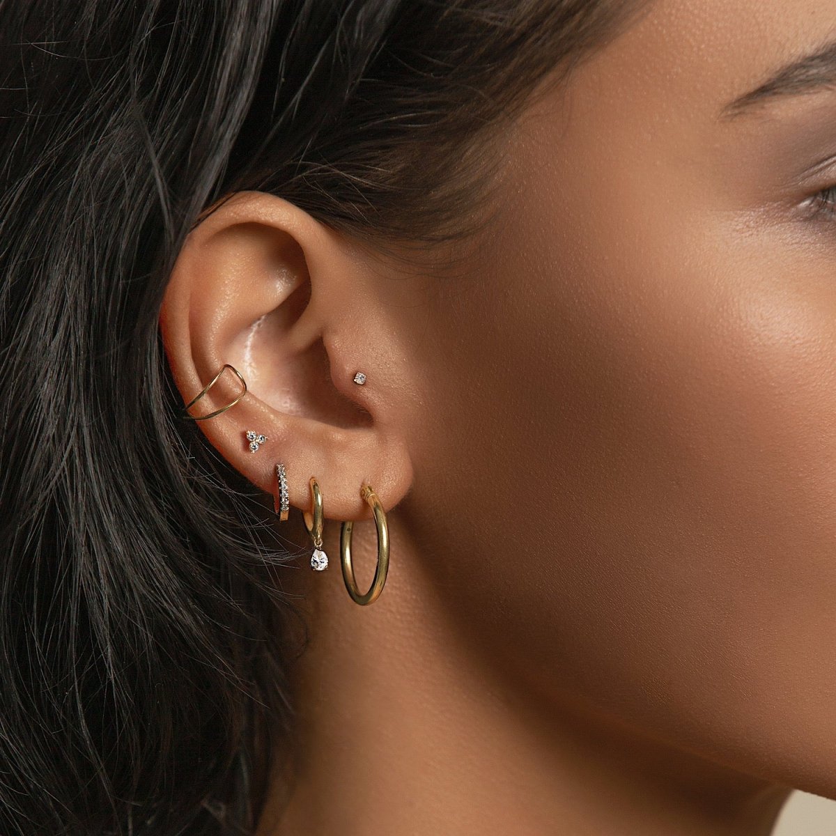 Gold ear cuff, pavé huggie, trio cluster, and dangle stud styled on a model's ear