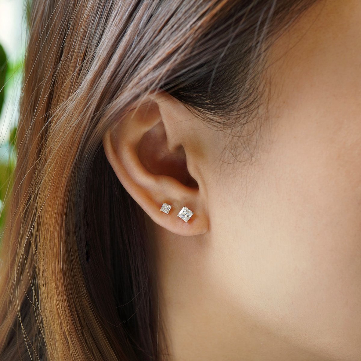 14K white gold princess-cut moissanite studs shown on a model's lobe in a small stack