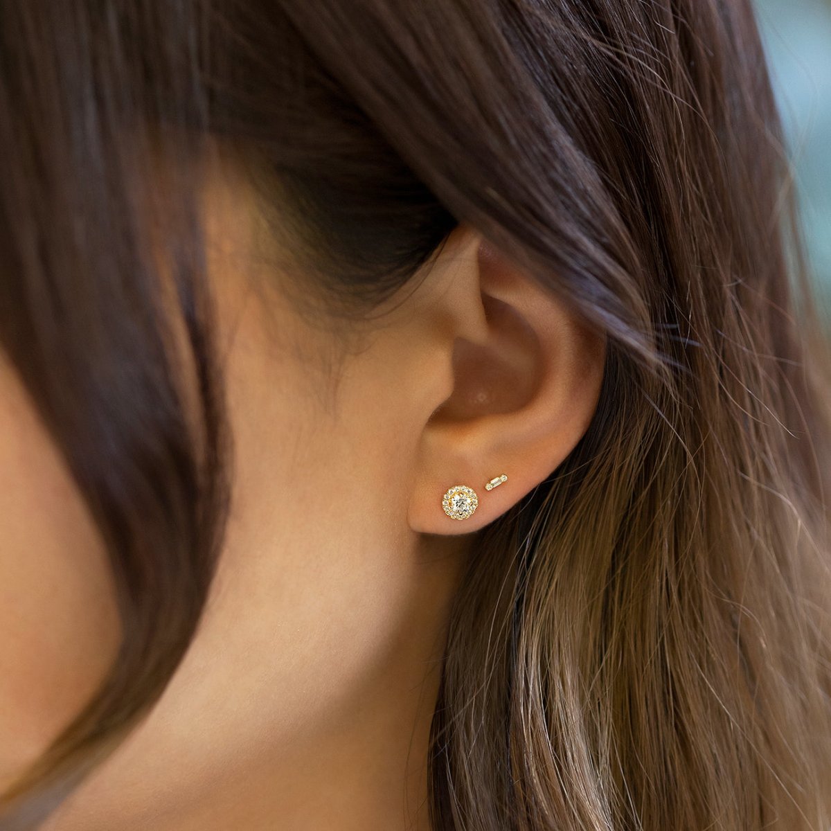 14K gold diamond baguette bar stud shown on a model's lobe beside a halo stud
