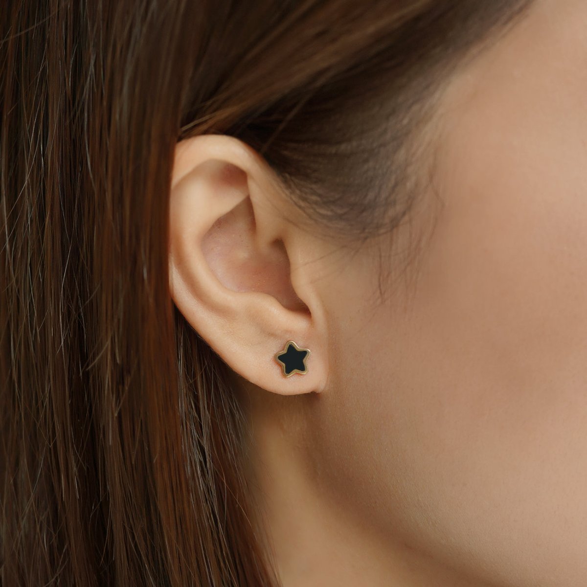 14K gold black onyx star stud shown on a model's earlobe