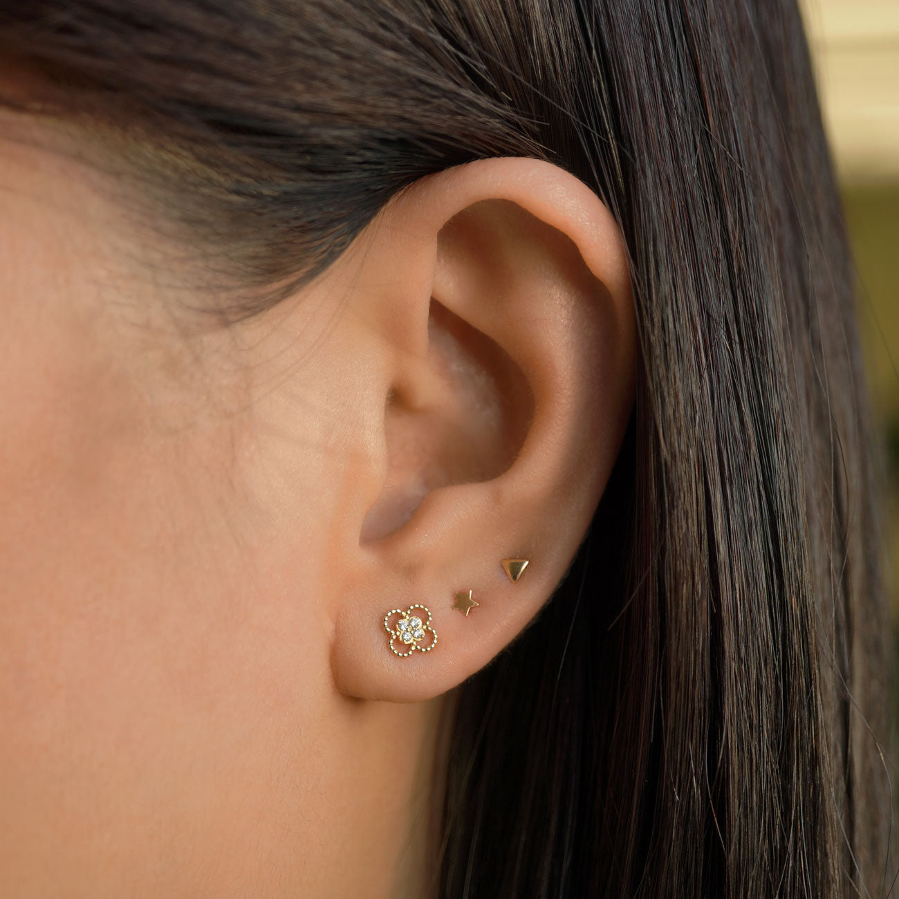 14K gold pavé flower, star and triangle studs styled in an ear stack on a model