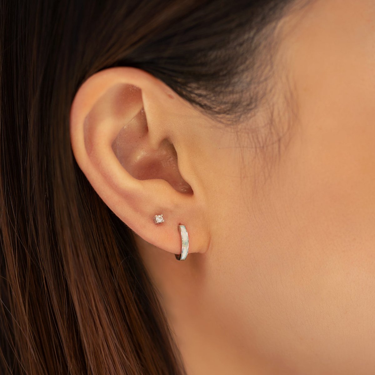 Sterling silver huggie hoop with light blue opal inlay, shown on a model's lower lobe
