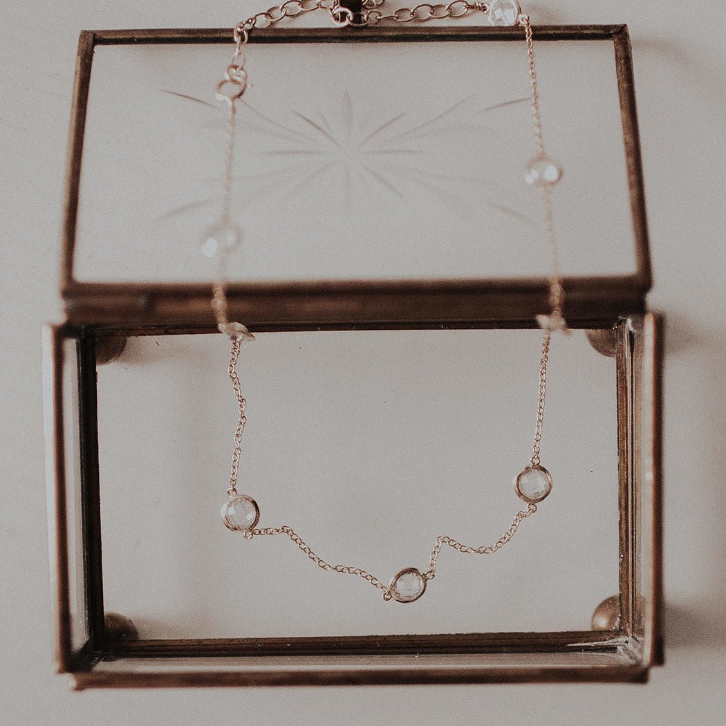 Gold vermeil white zirconia station choker draped over a glass box, styled flat