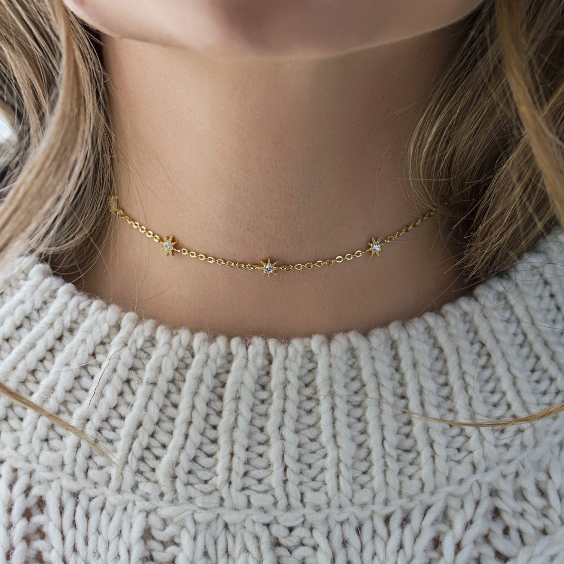 Gold vermeil starburst choker with white zirconia stars, shown on a model's neck over a knit sweater