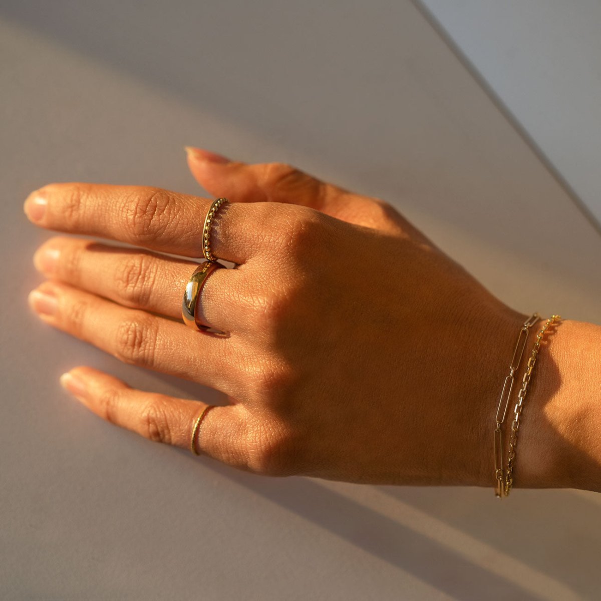 14K gold paperclip chain bracelet shown layered on a model's wrist beside a ring stack